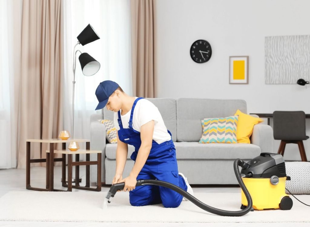 . A man in overalls uses a vacuum to clean a room, highlighting a carpet cleaning service based in Houston, TX.