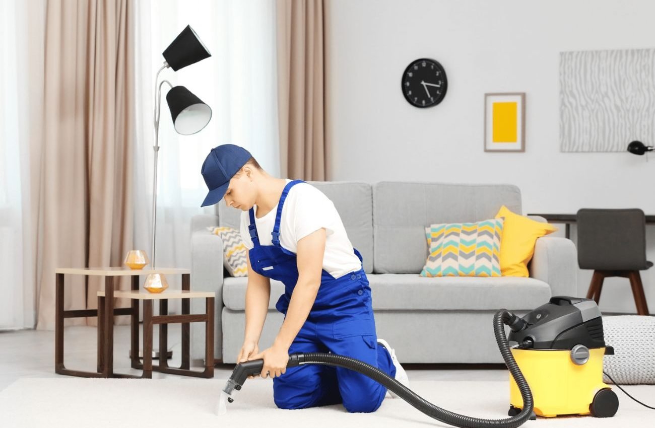 . A man in overalls uses a vacuum to clean a room, highlighting a carpet cleaning service based in Houston, TX.